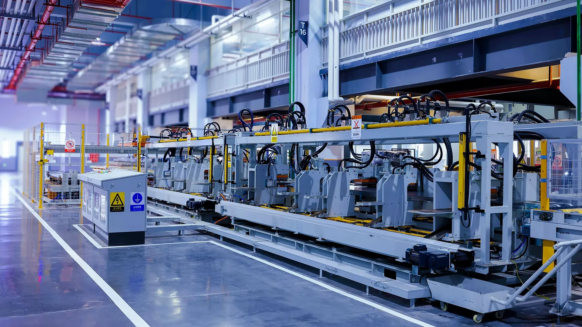 Industrial machinery, cables and yellow guard rails inside a large factory.